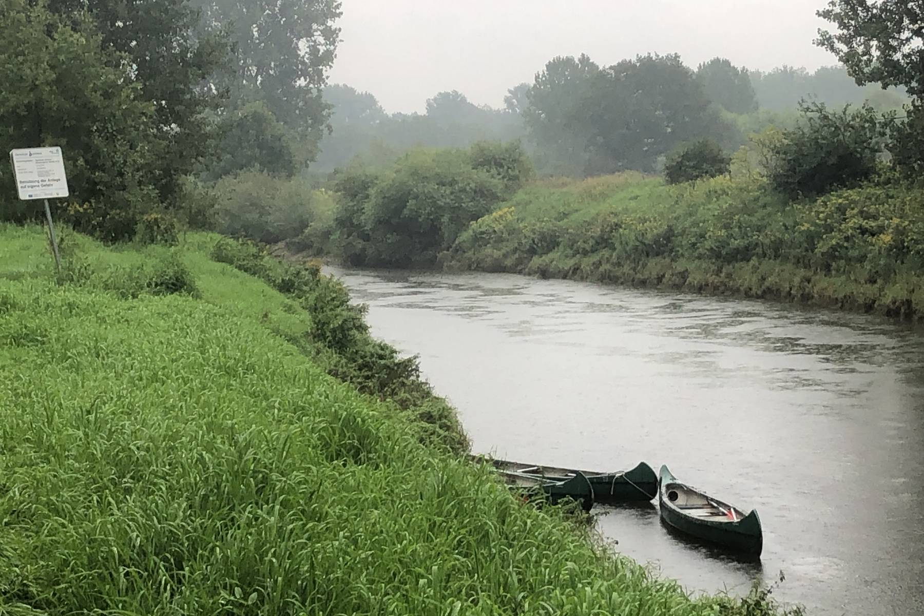 Blick vom Pausenstand unter der Brücke auf den Fluss mit den geparkten Kanus im Regen. Photo: Marcel (4|6)
